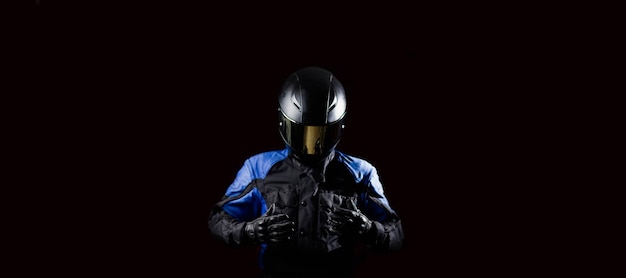 Motociclista motociclista em uma jaqueta protetora de motocicleta com luvas e um capacete em um fundo escuro.