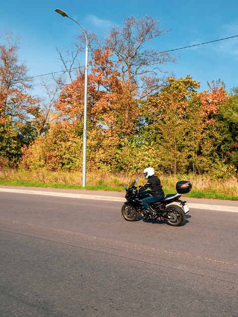 Motociclista en movimiento. Motorista en una motocicleta negra en el tráfico en un camino rural de otoño.