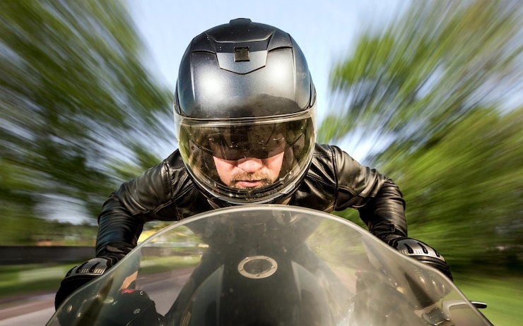 Foto motociclista no capacete e jaqueta de couro correndo na estrada.
