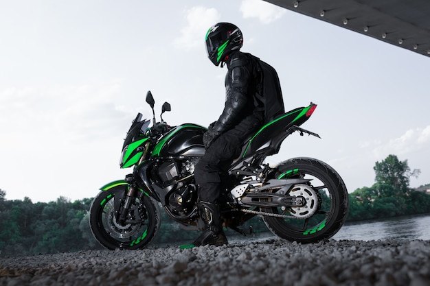 Foto motociclista parar debaixo da ponte sobre a estrada, esperando a chuva parar