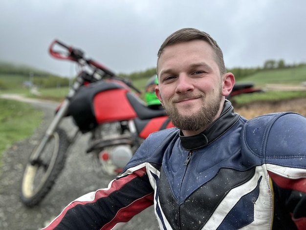 Un motociclista profesional descansando en un camino forestal después de un paseo aventurero y tomándose un selfie f