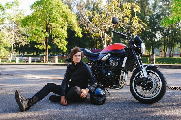 Motociclista sentado ao lado de sua motocicleta na estrada no parque