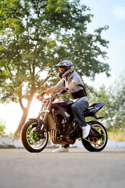 Foto motociclista sentado na motocicleta na rua ensolarada.