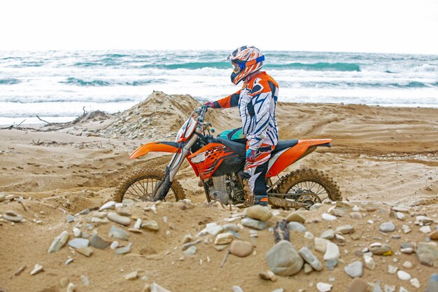 Foto motociclista en un traje de protección sentado en moto frente al mar