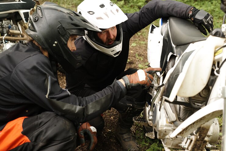 Foto motociclistas concentrados en cascos examinando la panza de la motocicleta mientras se discute el motivo de la avería