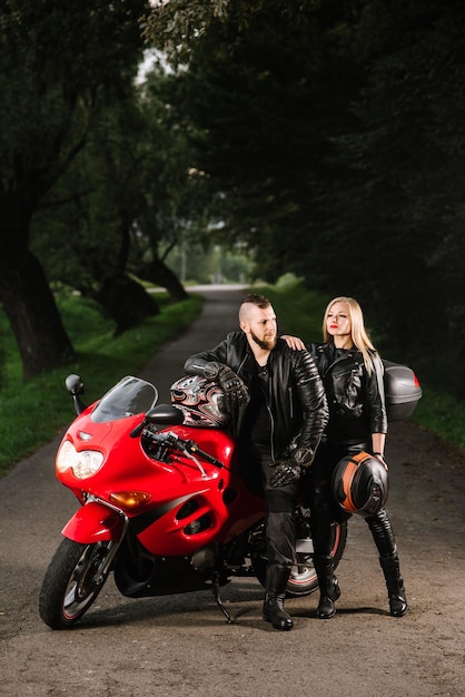 Foto motociclistas de hombre y mujer en chaquetas de cuero con moto deportiva en la carretera por la noche