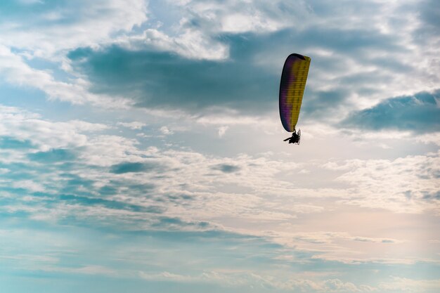 Motorgleitschirmfliegen im blauen Himmel mit weißer Wolke im Hintergrund.