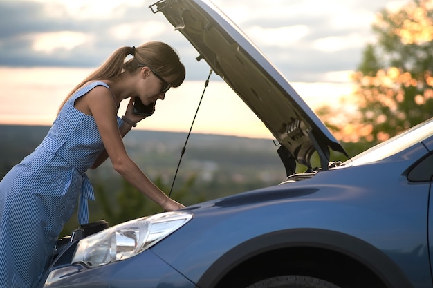 Motorista com raiva falando com raiva no celular com o trabalhador do serviço de assistência em pé perto de um carro quebrado com capô levantado enquanto inspecionava o motor tendo problemas com seu veículo.