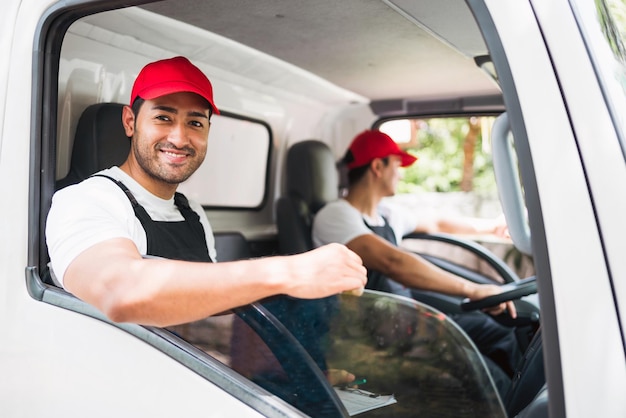 Motorista de caminhão profissional feliz com seu assistente vestindo um boné vermelho sorrindo olhando para a câmera