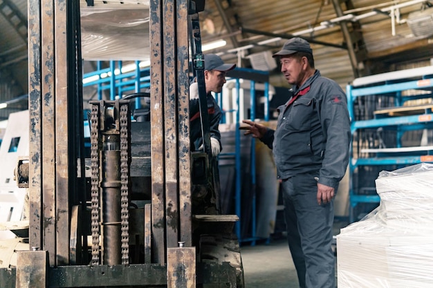 Motorista de empilhadeira e trabalhador em um armazém industrial em primeiro plano o mecanismo do carregador