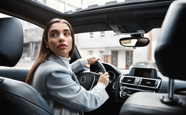 Motorista de empresária olhando para trás, carro no estacionamento. Mulher dirigindo ao contrário.