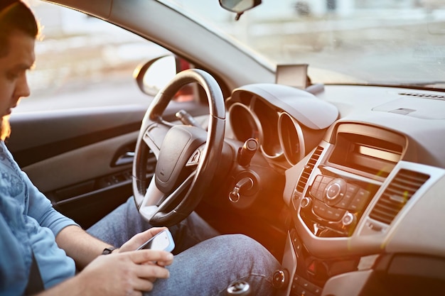 Motorista de homem usando telefone celular enquanto está sentado ao volante de um brilho do sol do carro