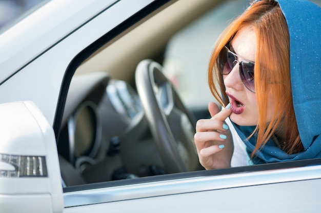 Motorista de mulher de negócios muito elegante cachecol e óculos de sol, verificando a maquiagem no espelho.