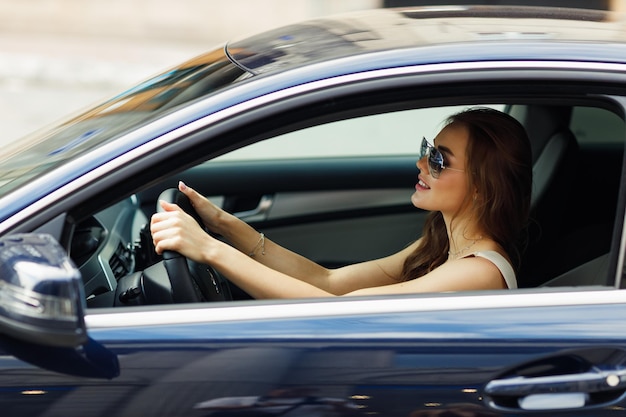 Motorista de mulher feliz em óculos de sol no carro sorrindo Linda jovem morena feliz dirigindo veículo de carro