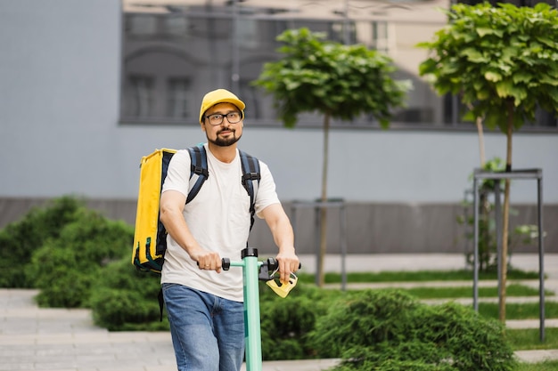 Motorista de scooter elétrico de entrega de comida com mochila amarela nas costas está a caminho para entregar comida