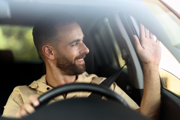 Foto motorista de táxi sorridente confiante acenando com a mão esperando o cliente sentado no carro. conceito de transporte