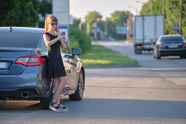 Motorista elegante em pé perto de seu veículo falando no celular na rua da cidade no verão