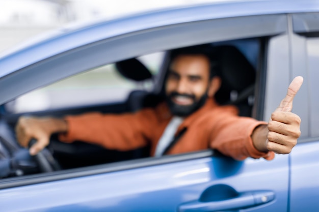 Motorista indiano feliz mostrando polegares para cima em automóvel novo