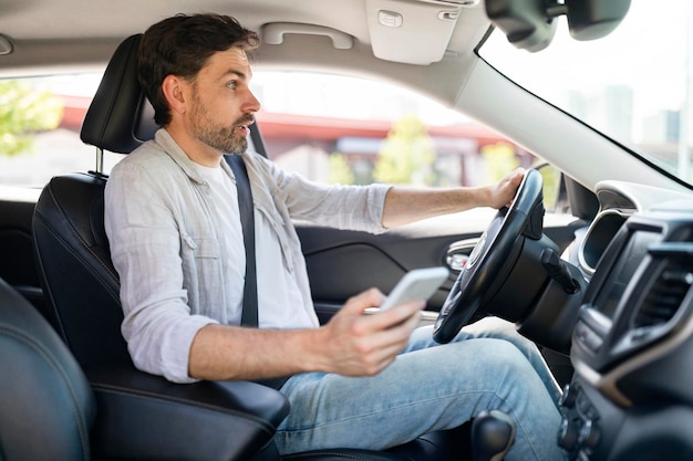 Motorista jovem chocado usando smartphone enquanto dirige o carro