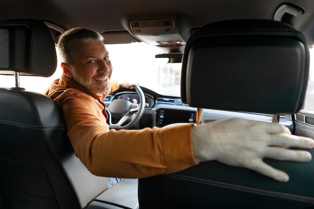 Motorista masculino de meia-idade positivo virando-se e olhando para trás para a câmera sentado em um novo carro de luxo