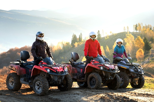 Motoristas felizes em capacetes de proteção, desfrutando de extrema equitação em motos de quadriciclo ATV nas montanhas de verão ao pôr do sol.