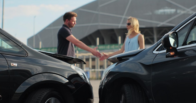 Motoristas homens e mulheres apertam as mãos após um pequeno acidente de viação Em primeiro plano há dois carros Final feliz em um pequeno acidente de viação Seguro de carro