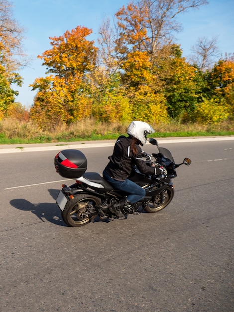 Motorradfahrer in Bewegung. Bikerin auf einem schwarzen Motorrad im Verkehr auf einer ländlichen Herbststraße.