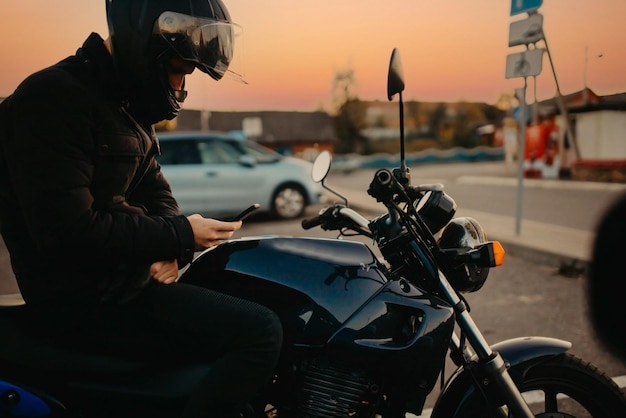 Motorradfahrer in Motorrad-Ausrüstung in der Nähe eines Motorrads bei Sonnenuntergang