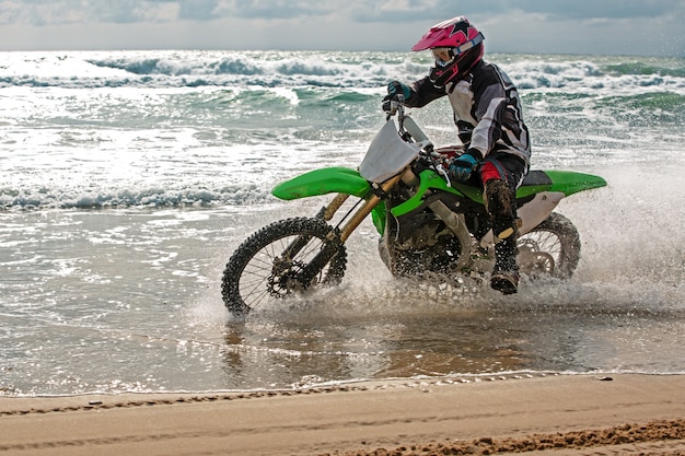 Motorradfahrer in Schutzanzug fährt Motorrad auf dem Meer, Spritzer fliegen unter den Rädern hervor.