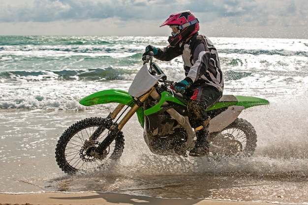 Motorradfahrer in Schutzanzug fährt Motorrad auf dem Meer, Spritzer fliegen unter den Rädern hervor.