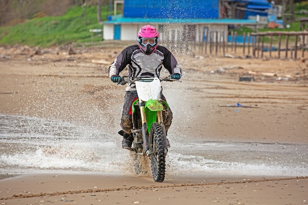 Motorradfahrer in Schutzanzug fährt Motorrad auf dem Meer, Spritzer fliegen unter den Rädern hervor.