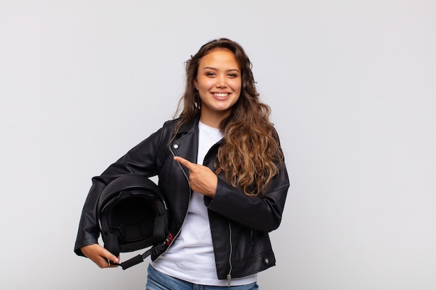 Motorradfahrerin der jungen Frau, die fröhlich lächelt, sich glücklich fühlt und zur Seite und nach oben zeigt und Objekt im Kopienraum zeigt