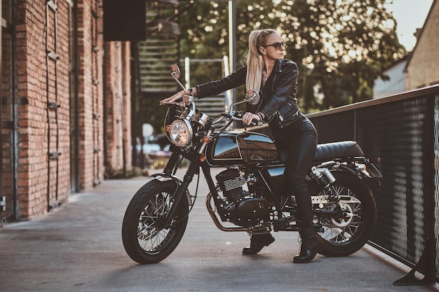 Motorradfahrerin in Volllederkombi posiert für Fotografen, während sie auf ihrem brandneuen Motorrad sitzt.