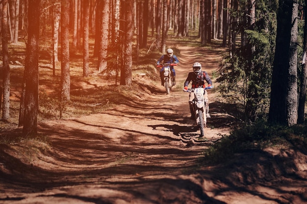 Motorradrennfahrer auf Enduro-Sportmotorrädern fahren bei einem Offroad-Rennen schnell auf einer staubigen Straße im Wald