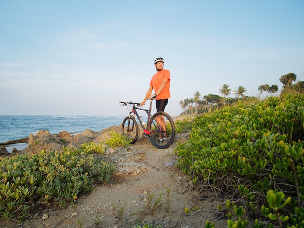 Mountainbiker steht mit Fahrrad am Ozeanufer.