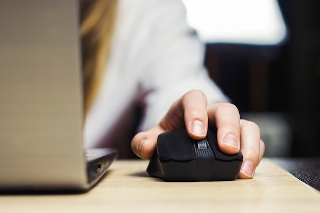 Mouse de computador em uma mão feminina, laptop em uma mesa de madeira. cena do ambiente de trabalho