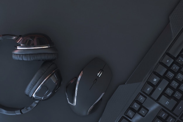 Mouse preto, teclado, fones de ouvido são isolados em um fundo escuro, a vista superior.