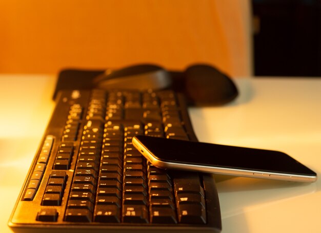 Un mouse y un teléfono celular en un teclado sobre una mesa blanca con una luz caliente