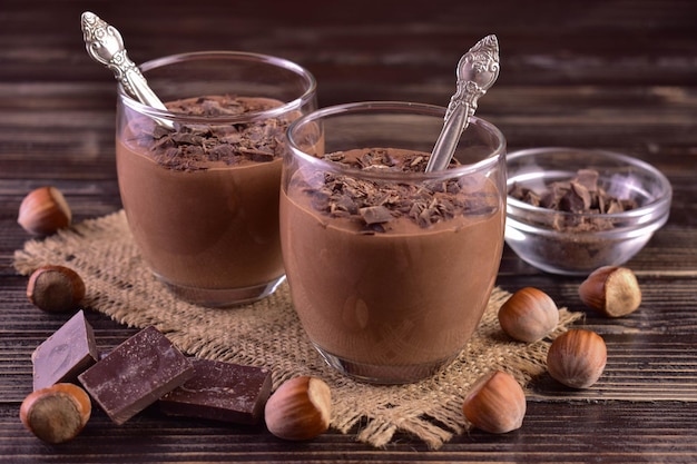 Mousse de chocolate amargo com avelãs em copos sobre um fundo escuro de madeira.