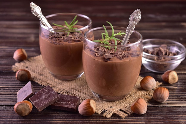 Mousse de chocolate amargo com avelãs em copos sobre um fundo escuro de madeira.