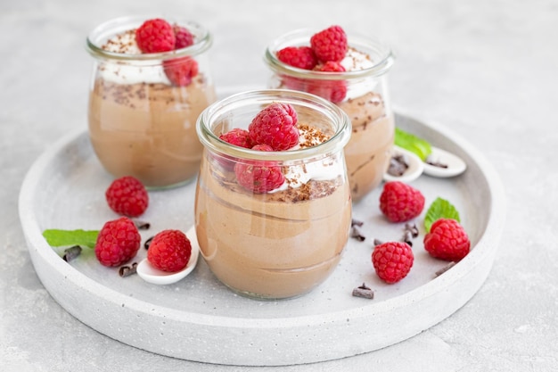 Mousse de chocolate com chantilly e framboesas frescas em um copo sobre fundo cinza de concreto