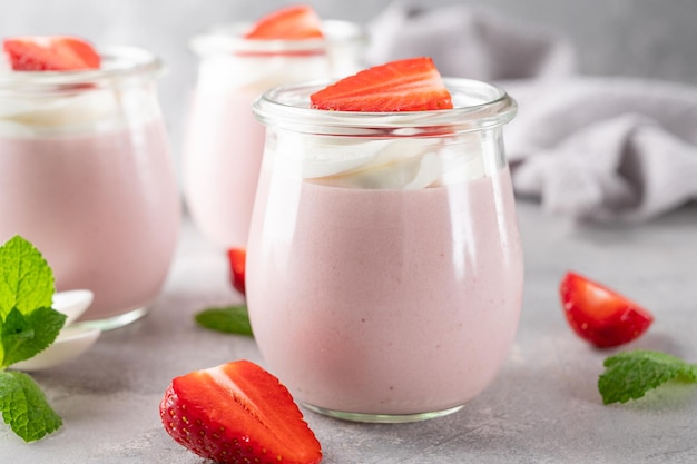 Mousse de morango em uma jarra de vidro em um fundo cinza de concreto com frutas de chantilly e hortelã