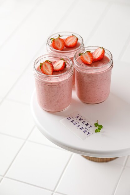 Mousse de tres postres de fresa en vidrio con adhesivo y menta en pizarra blanca sobre fondo de mosaico blanco