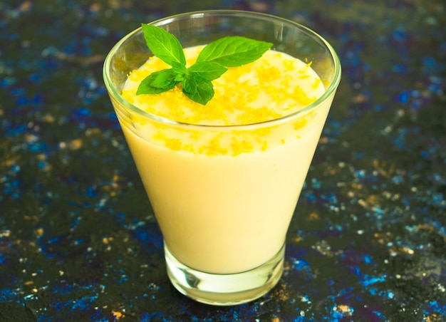 Mousse de vainilla o budín con ralladura de limón y menta en un vaso alto sobre un fondo azul oscuro