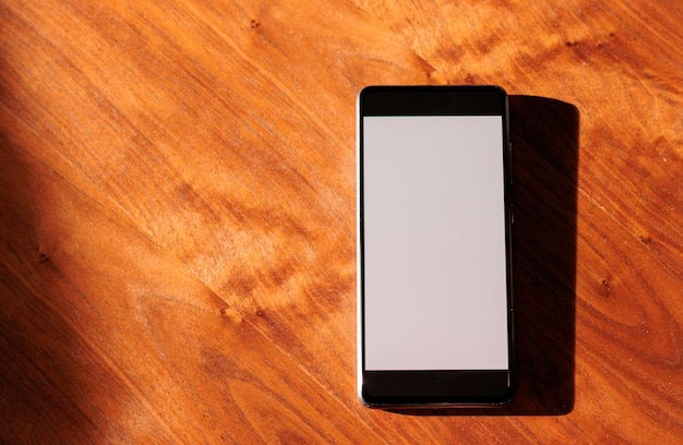 Móvil con pantalla en blanco sobre mesa de madera y luz natural