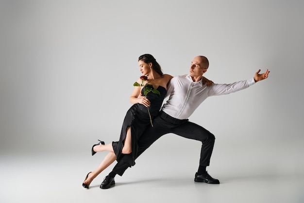 movimento de dança de jovem casal mulher morena segurando rosa vermelha e homem em trajes formais no estúdio