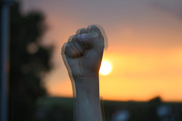 Foto movimento desfocado da mão recortada apertando o punho contra o céu durante o pôr do sol