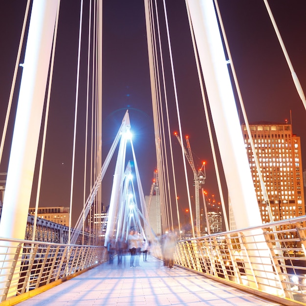 Foto movimento desfocado de pessoas em ponte suspensa iluminada à noite