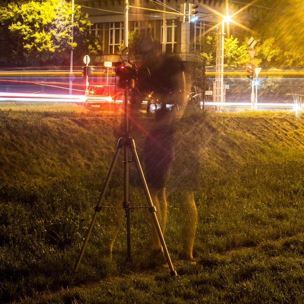 Foto movimento desfocado de um homem fotografando contra trilhas de luz à noite