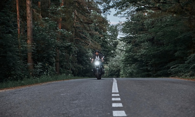 Movimento desfocado um jovem motociclista em um capacete monta rapidamente em alta velocidade em uma estrada florestal em movimento